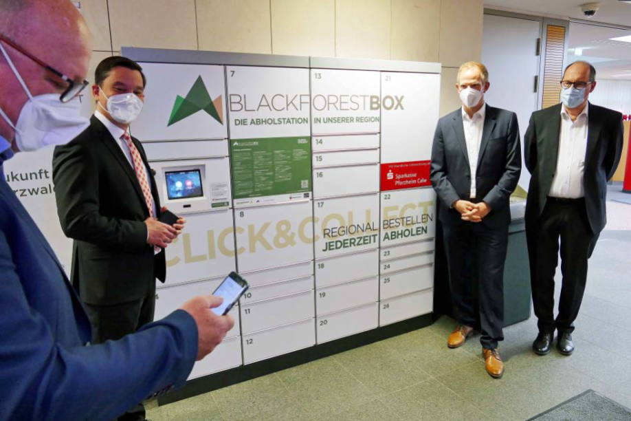 Mit der Abholstation BLACKFORESTBOX wie dieser in der Sparkasse Bad Wildbad will die Initiative DIGITAL BLACK FOREST dem regionalen  Einzelhandel unter die Arme greifen. Holger Frey (Modehaus Frey e.K. Bad  Wildbad), Klaus Mack (Bürgermeister Bad Wildbad und Verbandsvorsitzender  Regionalverband Nordschwarzwald), Dr. Matthias Proske (Verbandsdirektor Regionalverband Nordschwarzwald) und Stephan Scholl (Vorstandsvorsitzen- der Sparkasse Pforzheim-Calw) (v.l.n.r.) demonstrieren die Funktionsweise der BLACKFORESTBOX am Eröffnungstag. Foto: Regionalverband Nordschwarzwald. 